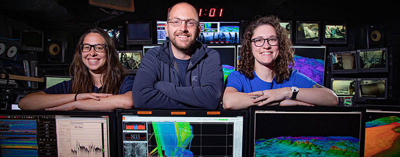 Two women and a man smiling for a picture in the control room of NOAA Ship Okeanos Explorer.